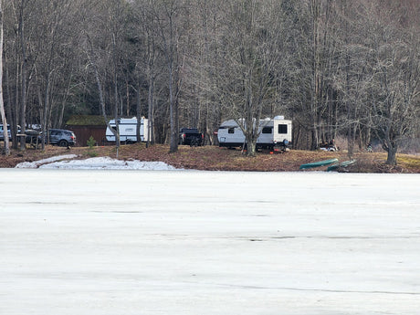 RVs and vehicles parked for winter camping by a frozen lake, surrounded by bare trees. An ideal rv rental adventure.