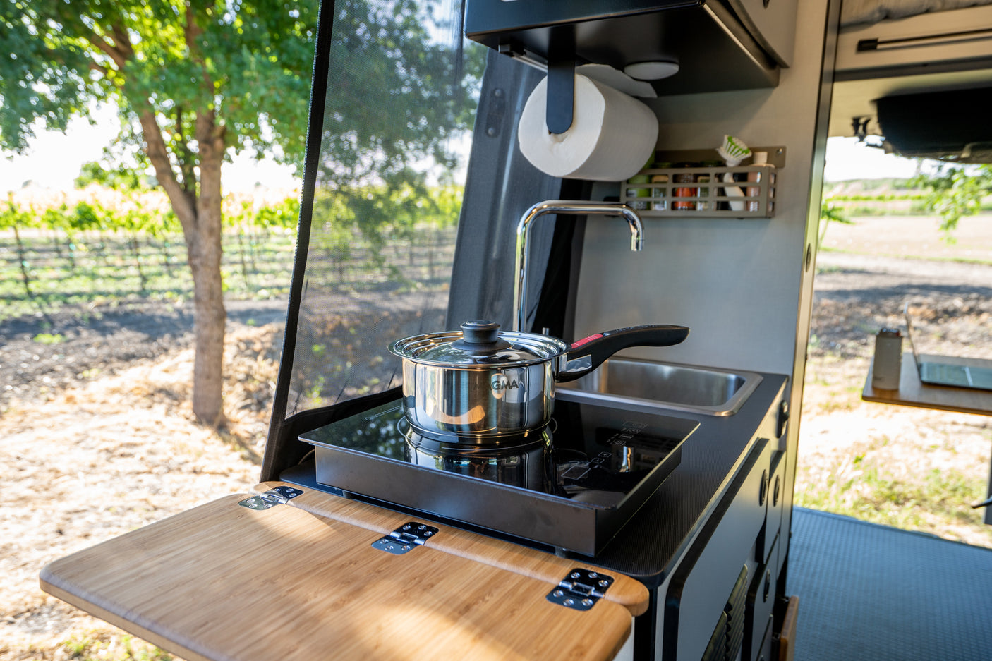 RV rental mobile kitchen setup: a pot on an induction cooktop, sink, and folding counter, with a scenic outdoor view.