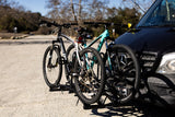 Two mountain bikes on a front hitch rack of a black RV rental van, ready for outdoor adventure.