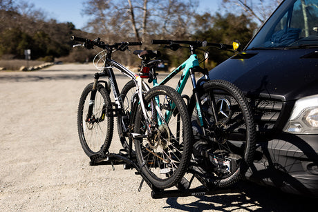 Two mountain bikes on a front hitch rack of a black RV rental van, ready for outdoor adventure.