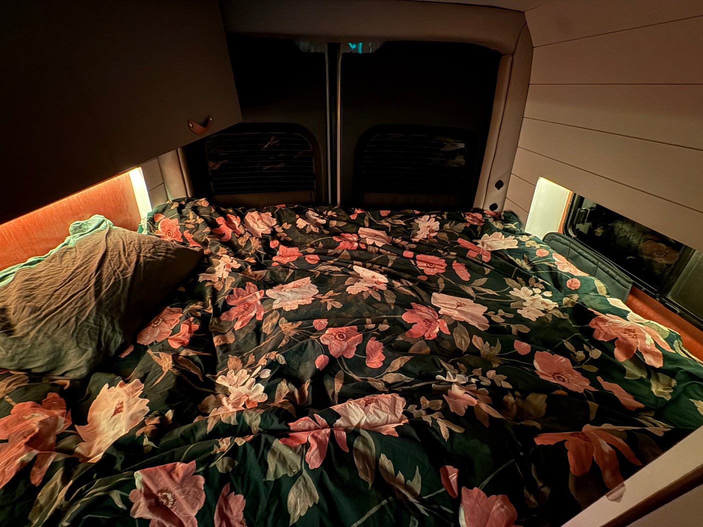 A comfortable floral bed in an rv rental van, illuminated by warm lighting, inviting for travel adventures.