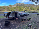An RV rental teardrop camper and minivan set up at a scenic mountain campsite.