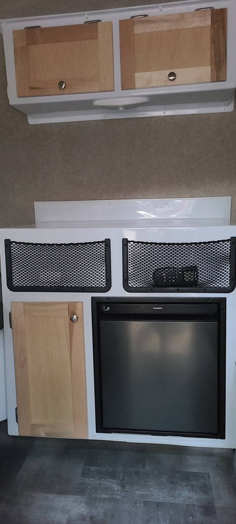 RV rental interior features light wood cabinets, mesh storage pockets, a lower cabinet, and a built-in Dometic refrigerator.
