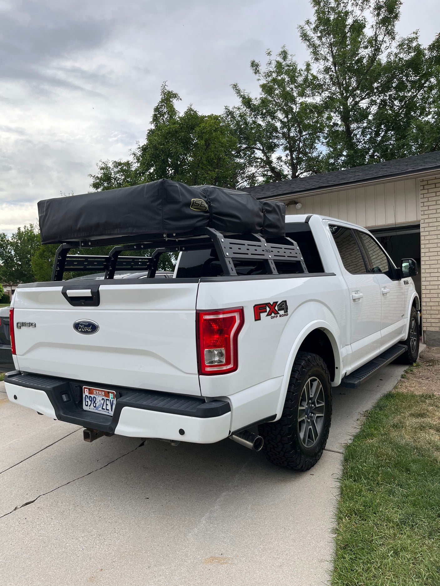 White Ford F-150 truck equipped with an RCI bed rack and black rooftop tent, offering a unique RV rental experience.