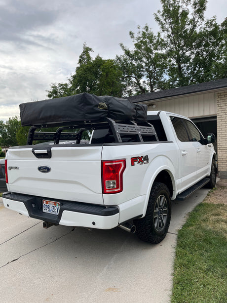 White Ford F-150 truck equipped with an RCI bed rack and black rooftop tent, offering a unique RV rental experience.