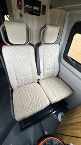 RV rental interior showing two cream-colored quilted passenger seats, a solar charge controller, and wood-grain paneling.