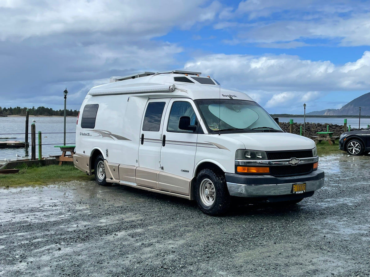 White Roadtrek RV rental parked on wet gravel by a bay — photo 1