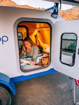 Woman reads in a cozy GoLoop RV rental. Experience comfort in a compact travel trailer, perfect for your next adventure.