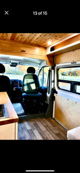 Interior view of an rv rental showing front cab, kitchen, and wooden ceiling. Autumn scenery outside.