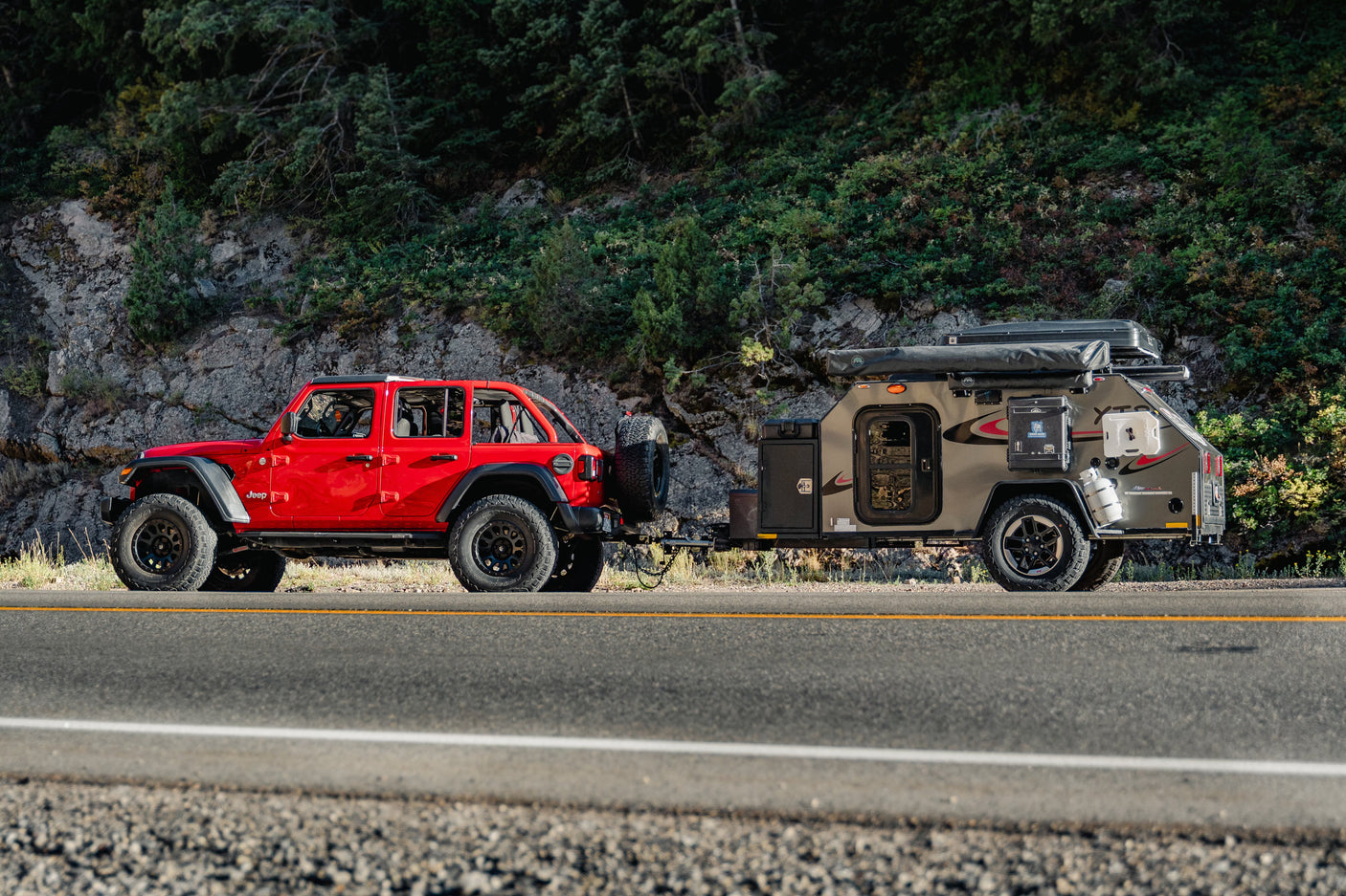 A vibrant red Jeep Wrangler tows a rugged off-road RV trailer on a scenic mountain road. Perfect for your next RV rental adventure.