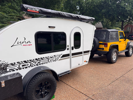 White Luna Rover teardrop trailer hitched to a yellow Jeep Wrangler, ready for an RV rental adventure.