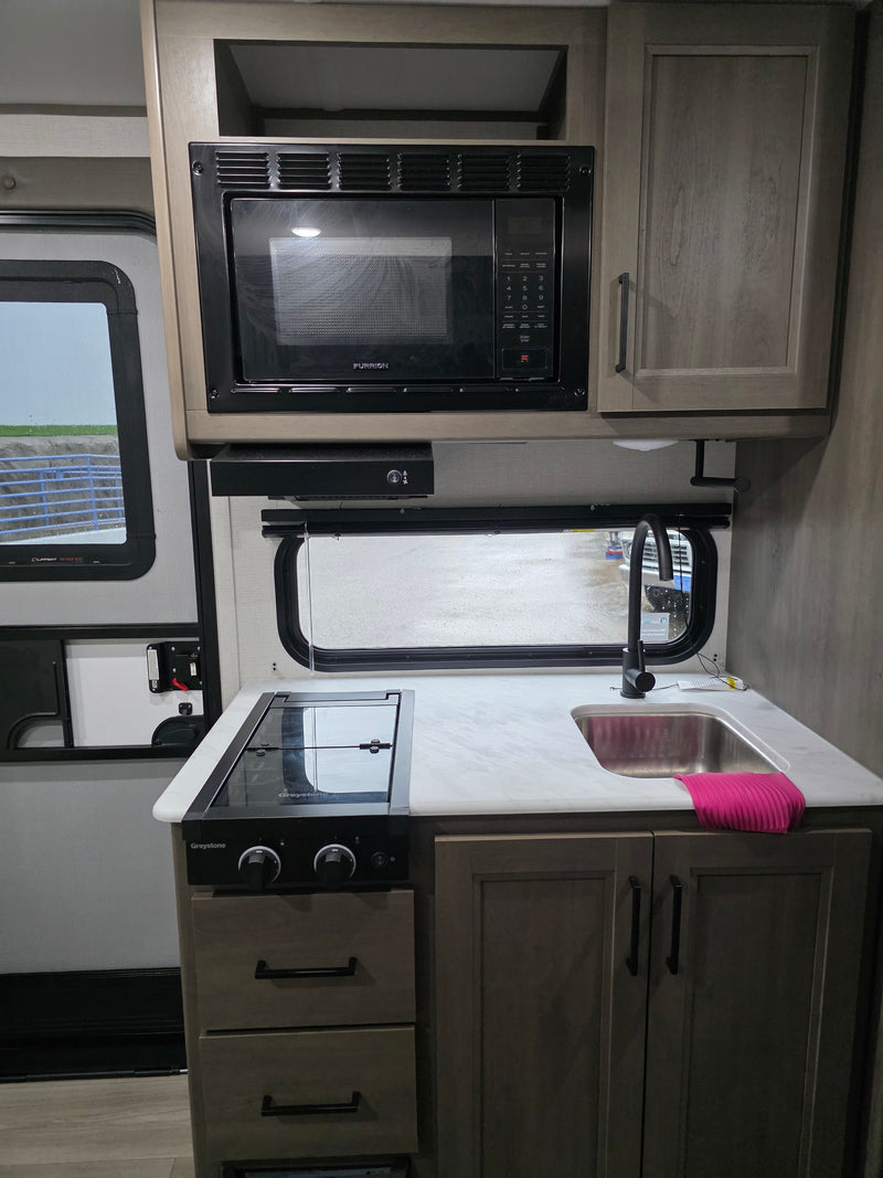 This RV rental kitchen features a Furrion microwave, Greystone stovetop, sink, and cabinets, offering a compact and functional space for travel. — photo 7
