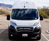 This white Winnebago RV rental van, a Ram ProMaster, is parked in a rugged desert mountain landscape, ready for adventure.