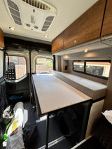 Spacious RV rental interior with a versatile table/bed, comfy bench seating, overhead AC, and storage for road trips.