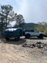 Explore with this RV rental: Grey Ford Bronco towing a green teardrop camper at a mountain campsite.