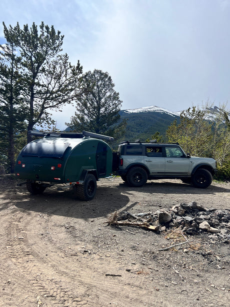 Explore with this RV rental: Grey Ford Bronco towing a green teardrop camper at a mountain campsite.