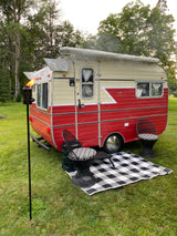 This charming vintage **RV rental** offers an inviting outdoor space with chairs, a checkered mat, and a tiki torch.
