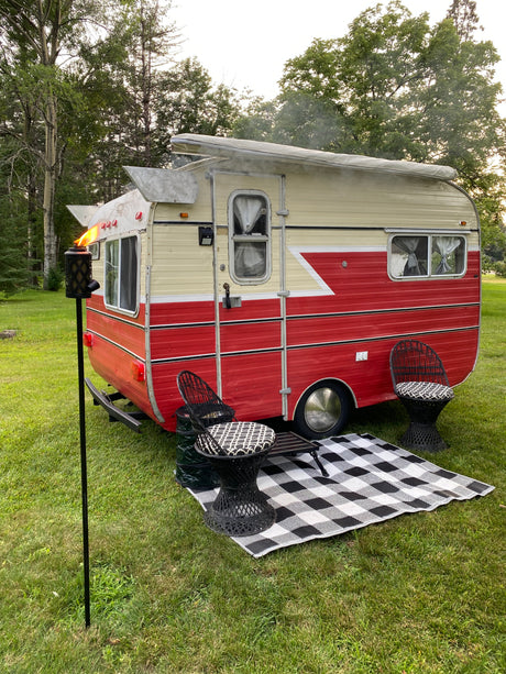 This charming vintage **RV rental** offers an inviting outdoor space with chairs, a checkered mat, and a tiki torch.