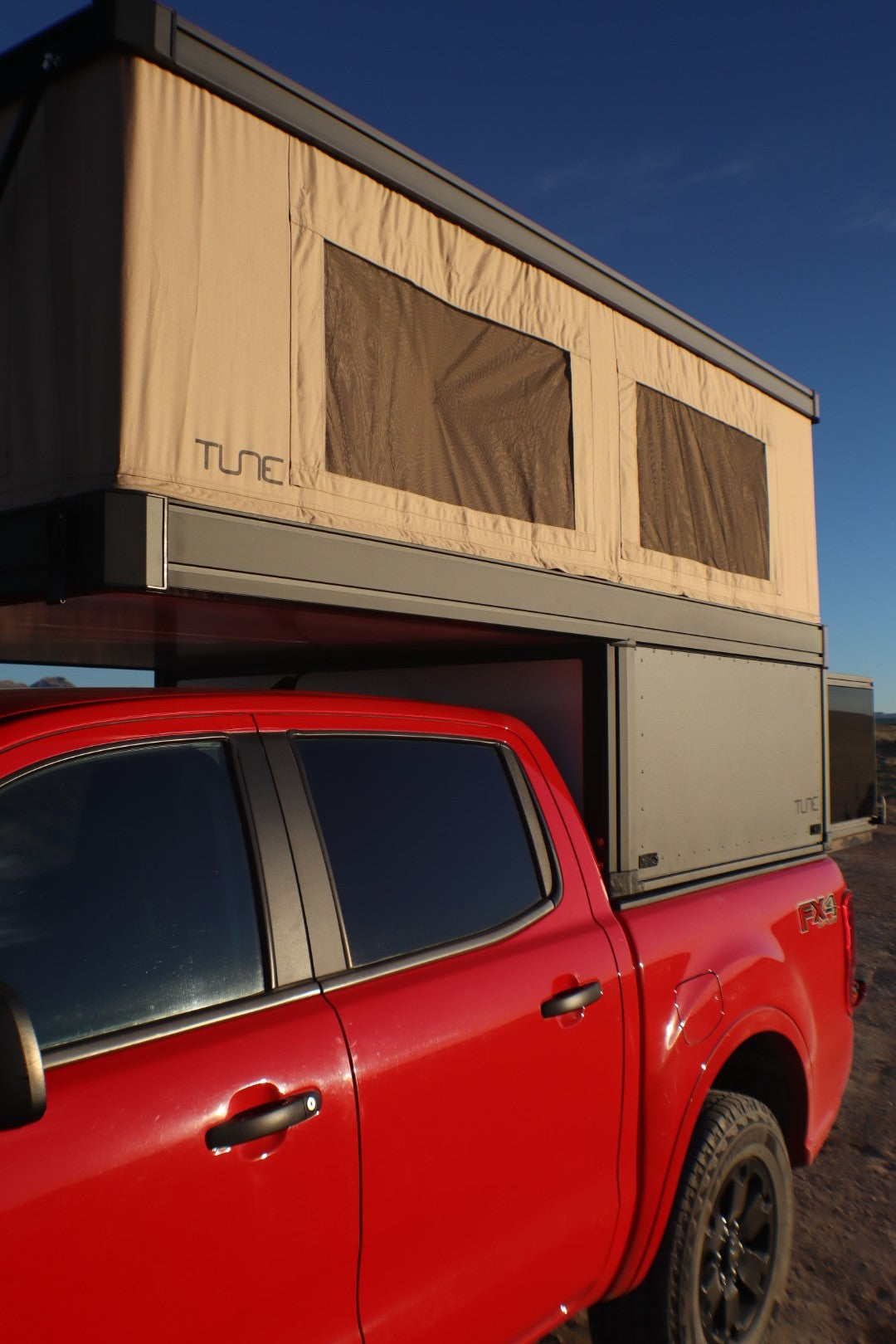 Red pickup truck with a beige Tune pop-up truck bed camper. Ideal RV rental for outdoor adventures.