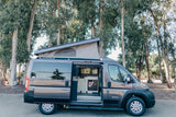 Gray Ram ProMaster pop-top camper van with open side door showing kitchenette. Perfect RV rental for adventures.