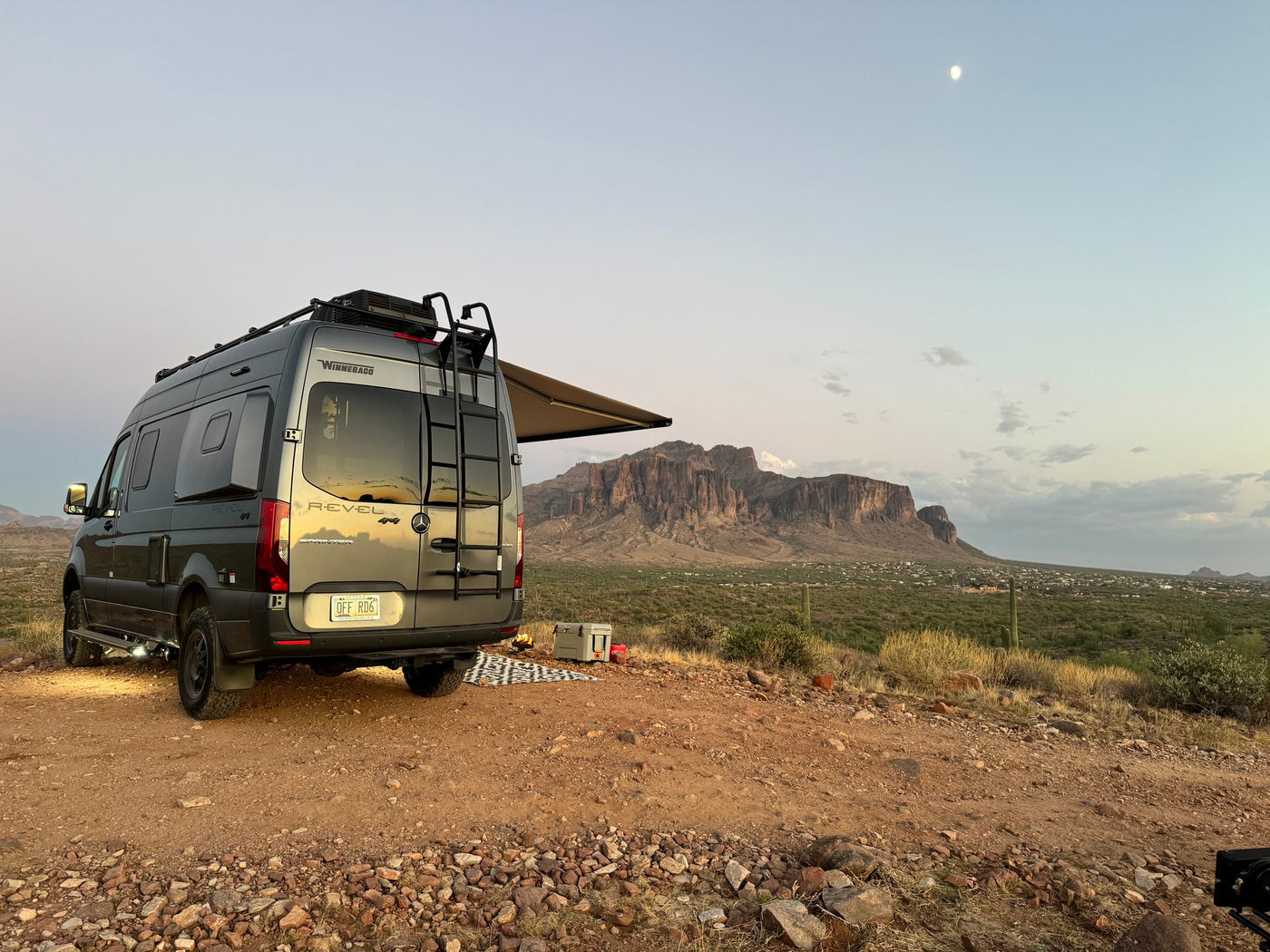  and outdoor living area.|RV rental adventure: Enjoying cocktails & chips with a blender setup and stunning desert mountain views from inside a camper van.|RV rental campervan parked in desert with mountains — photo 3