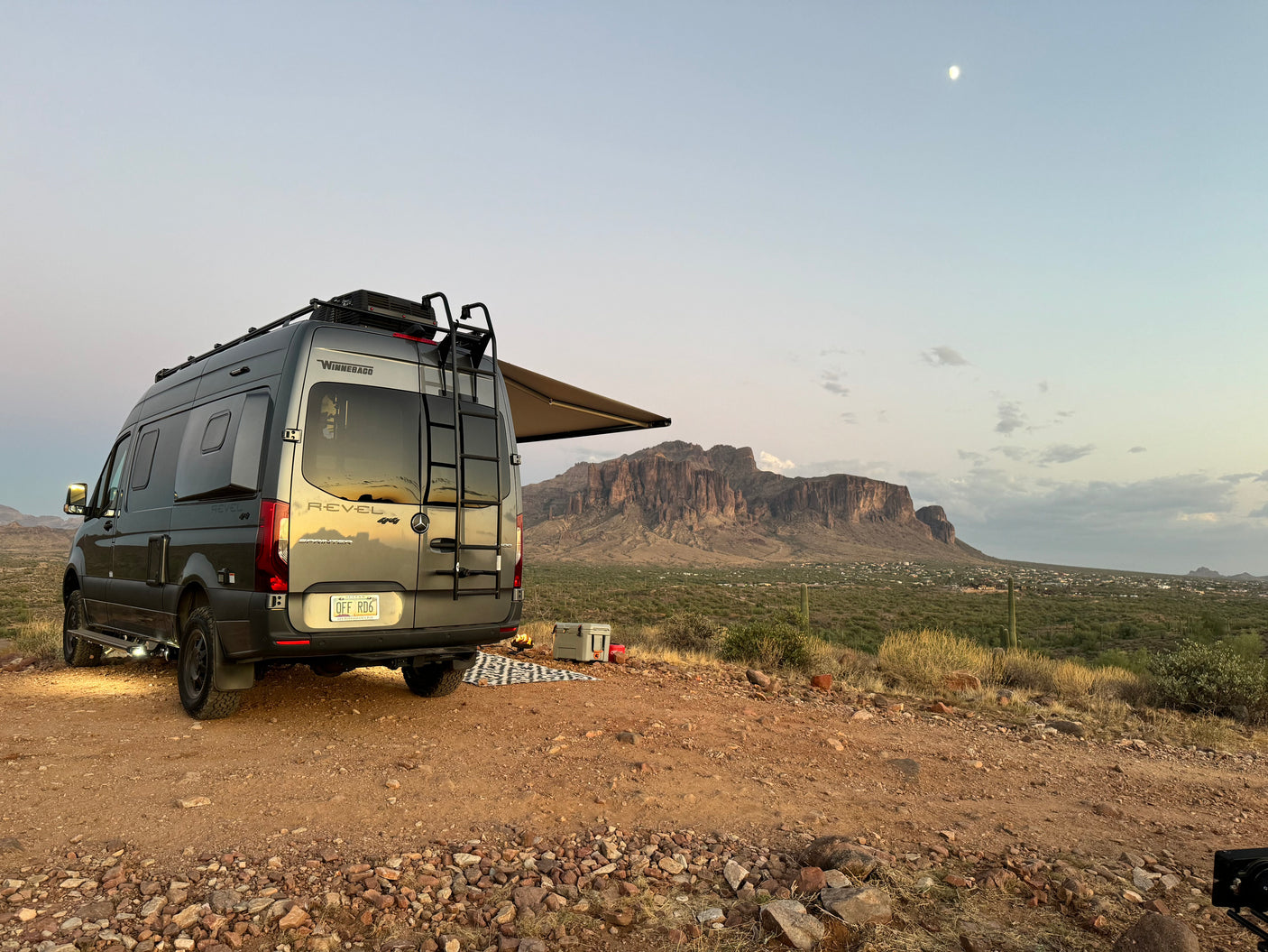 RV rental campervan parked in desert with mountains, cooler, campfire, and moonlit sky. Ideal for adventure and boondocking.