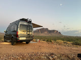 RV rental campervan parked in desert with mountains, cooler, campfire, and moonlit sky. Ideal for adventure and boondocking.