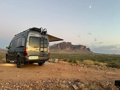 RV rental campervan parked in desert with mountains, cooler, campfire, and moonlit sky. Ideal for adventure and boondocking.