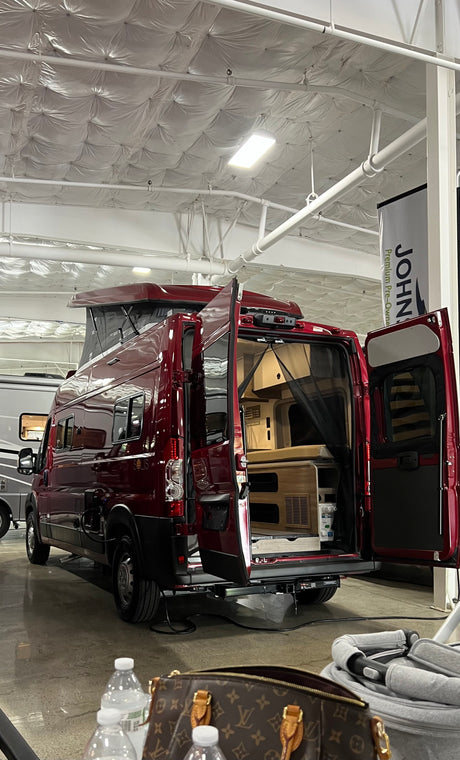 This vibrant red pop-top RV camper van, with its rear doors open revealing the living space, is ready for an RV rental.