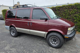 Maroon and tan Chevy Astro van, equipped with a roof rack and all-terrain tires. Perfect for your next RV rental adventure.
