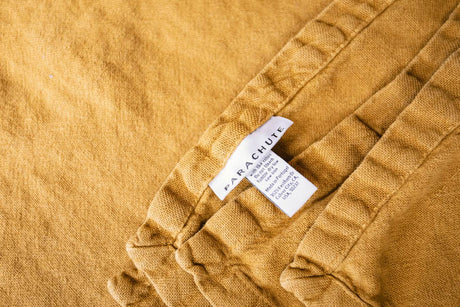A cozy Parachute blanket in mustard yellow, ideal comfort for your next RV rental trip. Care tag details visible.