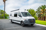 White Mercedes-Benz Sprinter RV rental van from Motobox, equipped with an awning, parked outdoors.