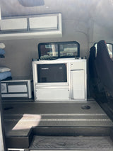 RV rental interior: A Dometic fridge built into white modular storage, alongside upholstered grey walls & textured floor.