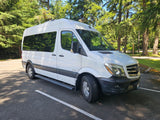 A white Mercedes Sprinter van, ideal for rv rental, is parked in a sunny wooded area. Perfect for outdoor adventures.