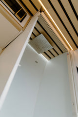 Modern RV rental shower featuring a large rain shower head, wooden slatted ceiling, and integrated LED lighting.