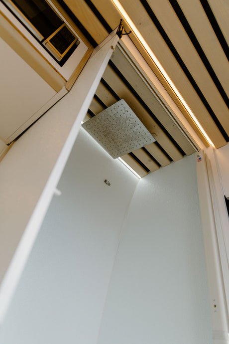Modern RV rental shower featuring a large rain shower head, wooden slatted ceiling, and integrated LED lighting.