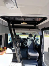 RV rental interior showing front cabin, dashboard, and ladder to a pop-top bed. A smoke alarm is visible on the ceiling.
