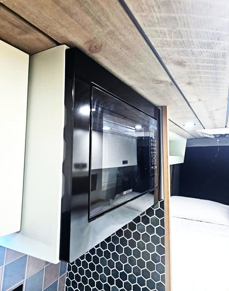 Stylish RV rental kitchen featuring a black microwave, honeycomb tile backsplash, and a modern wood plank ceiling.