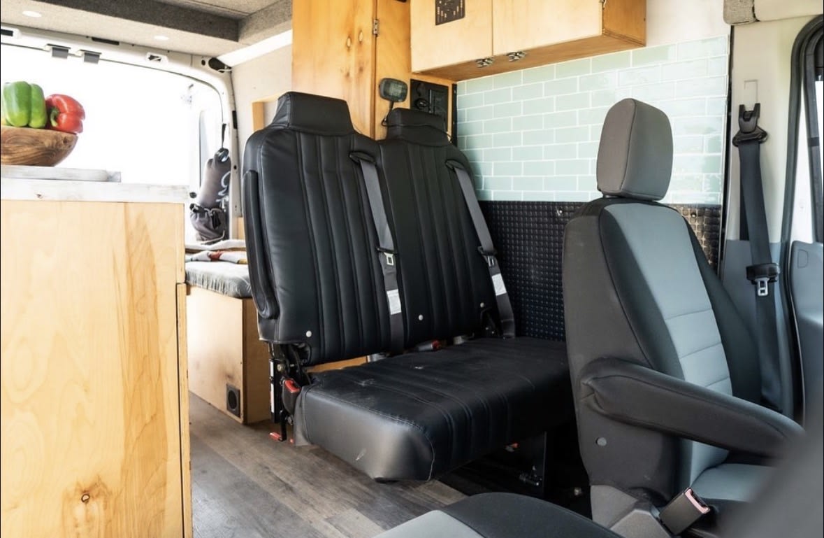 Inside this RV rental: black bench seating with seatbelts, a wooden kitchen area, and a tiled wall. Ideal for travel. — photo 7