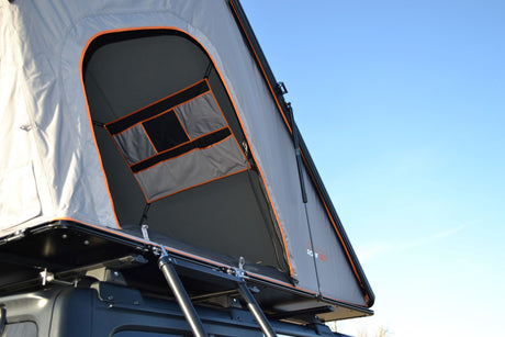 Grey rooftop tent open on vehicle roof, revealing orange trim & interior storage. Perfect for RV rental adventure.