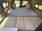 This RV rental offers a comfortable sleeping and seating area with a bed, cushions, and stylish wood paneling.