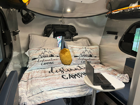 Cozy RV rental interior featuring a 'Destination Camping' bed, laptop table, and integrated amenities.