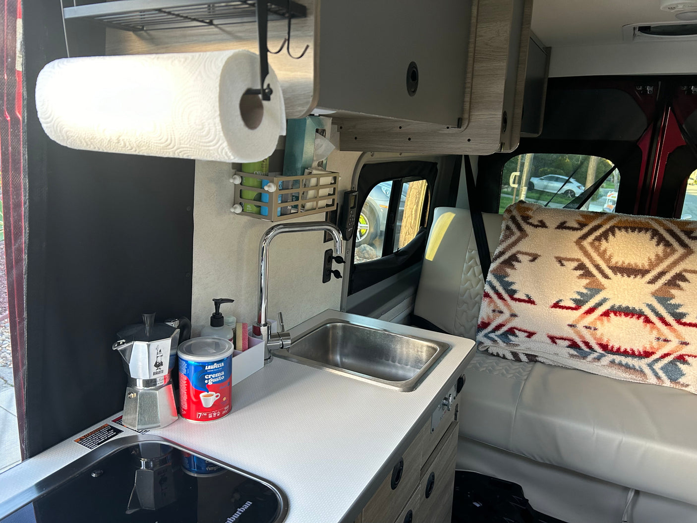 Inside a cozy RV rental kitchen with sink, coffee maker, paper towels, and storage solutions.
