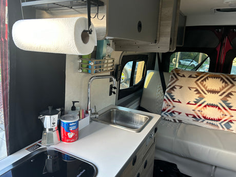 Inside a cozy RV rental kitchen with sink, coffee maker, paper towels, and storage solutions.