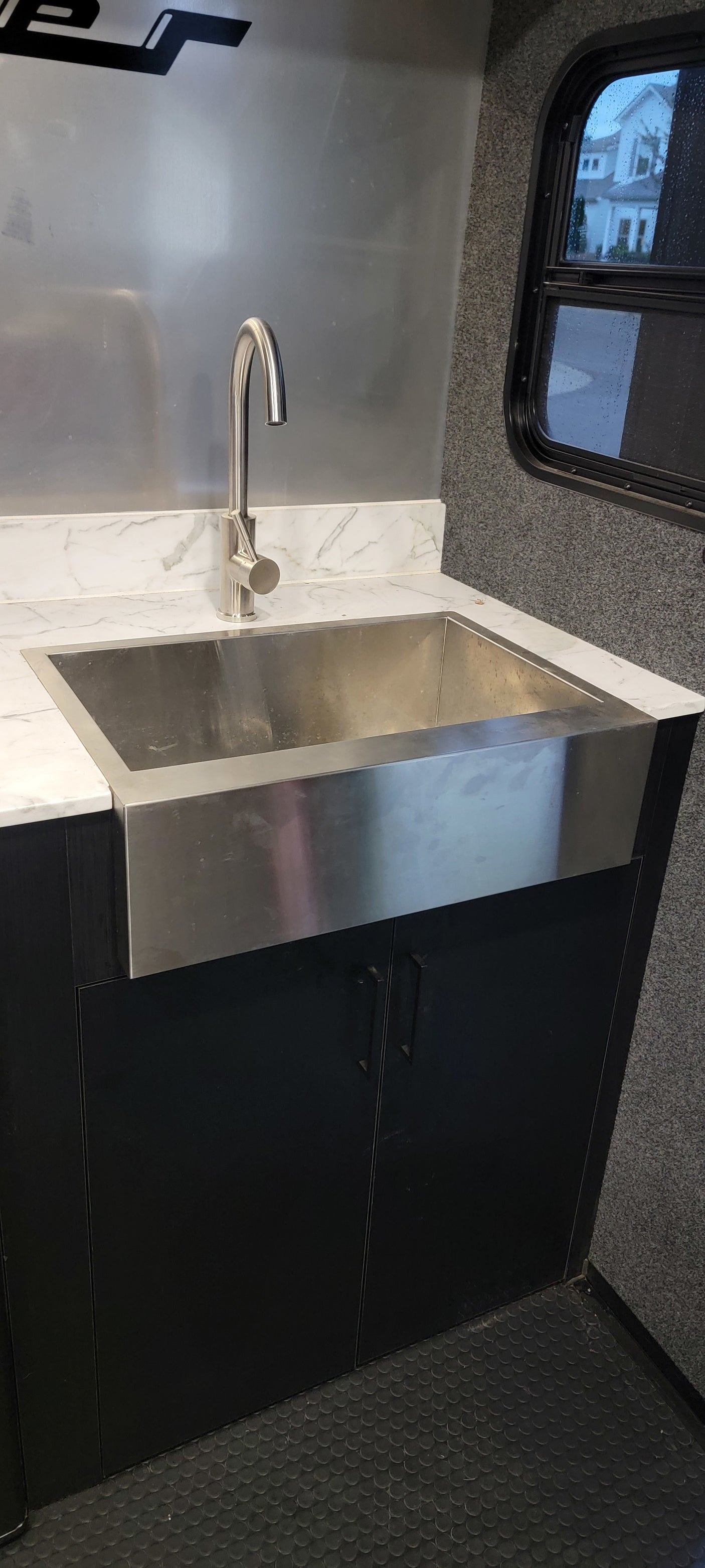 RV rental: Modern kitchen with a stainless steel farmhouse sink, sleek faucet, white marble counter, and black cabinets.