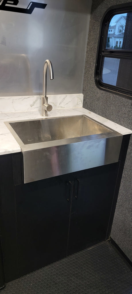 RV rental: Modern kitchen with a stainless steel farmhouse sink, sleek faucet, white marble counter, and black cabinets.