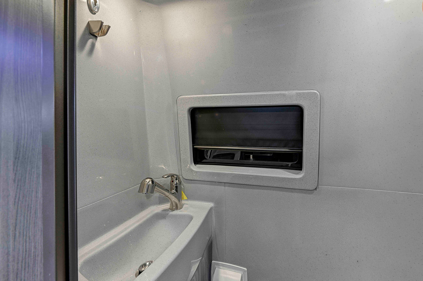 Modern RV rental wet bath featuring a speckled sink, chrome faucet, and privacy window with shade.