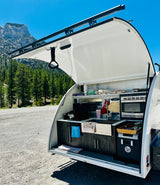 Open rear kitchen of an RV rental teardrop trailer, ready for outdoor cooking amidst mountain scenery.