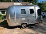 A sleek silver Airstream travel trailer, perfect for an RV rental, is parked on a gravel lot under a clear sky.