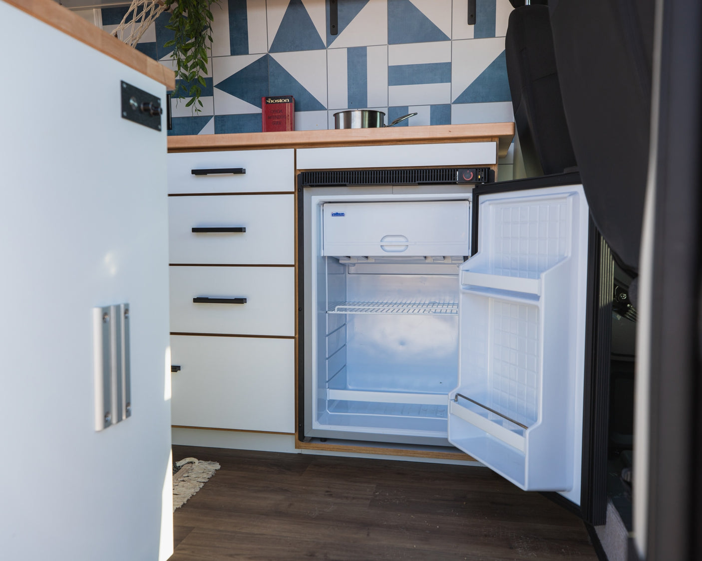 Modern RV rental interior showing a compact, open refrigerator, ample storage, and stylish tiled backsplash.